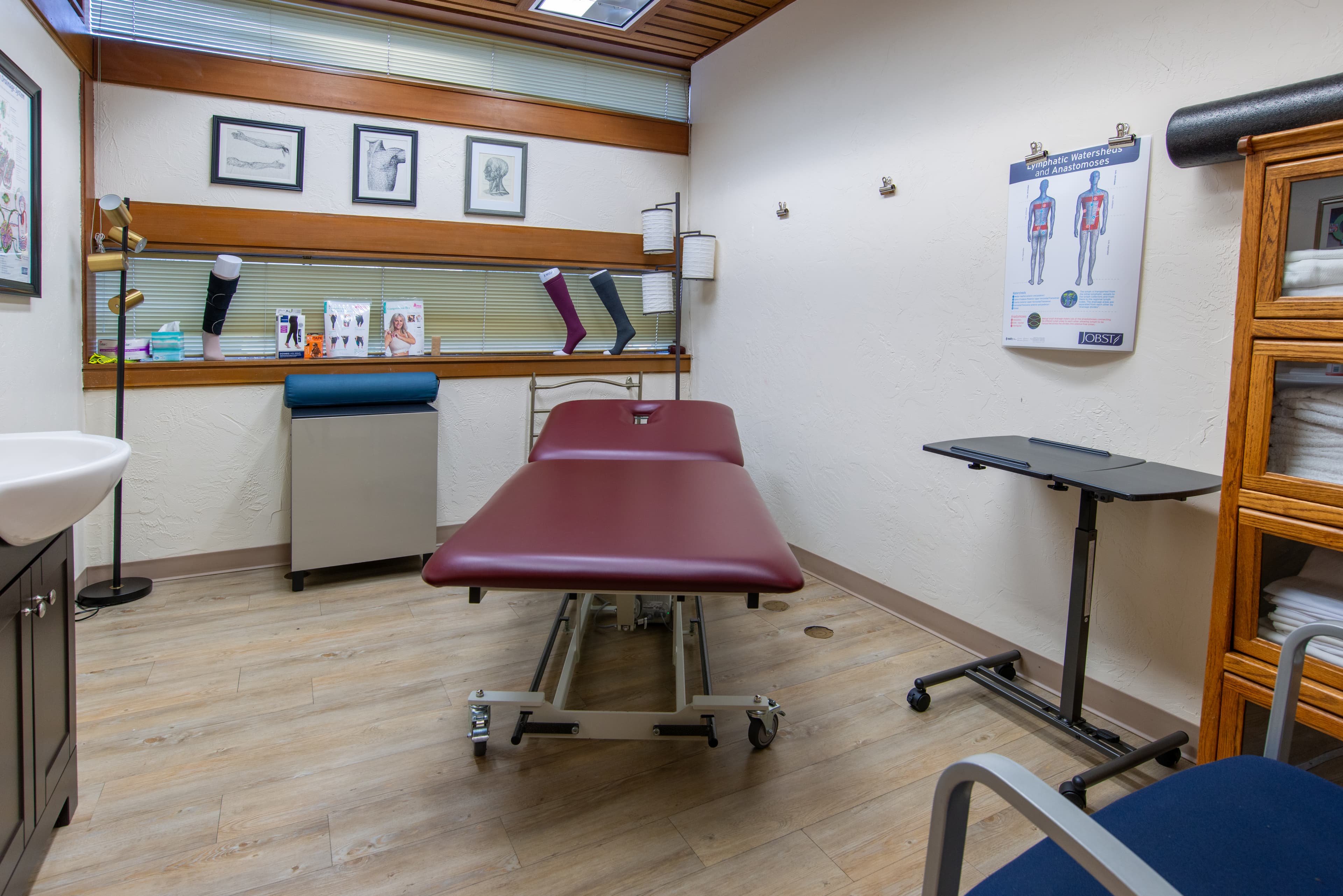 A private treatment room with a treatment bed and a bariatric chair, anatomical references and demonstrations of compression socks adorn the room.